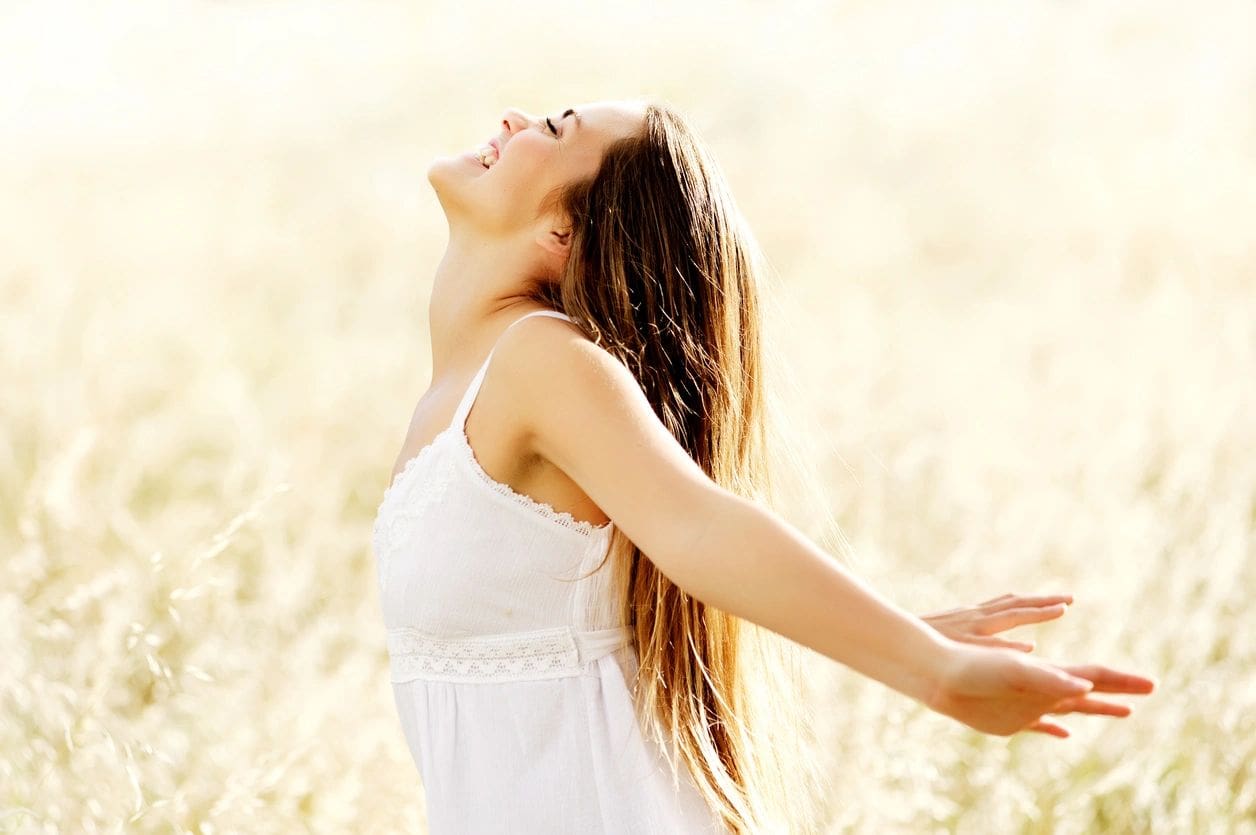 Woman in white dress enjoying nature with arms outstretched.
