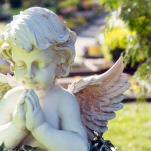 A white angel statue praying in a garden.