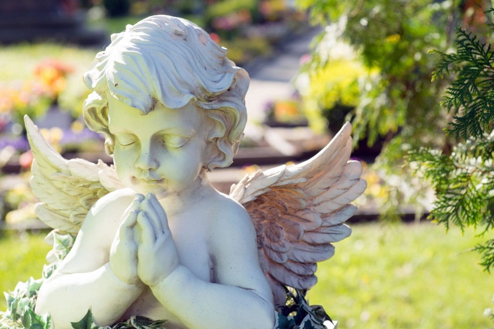 A white angel statue praying in a garden.