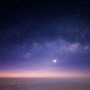 Starry night sky with a bright celestial object and a colorful horizon.