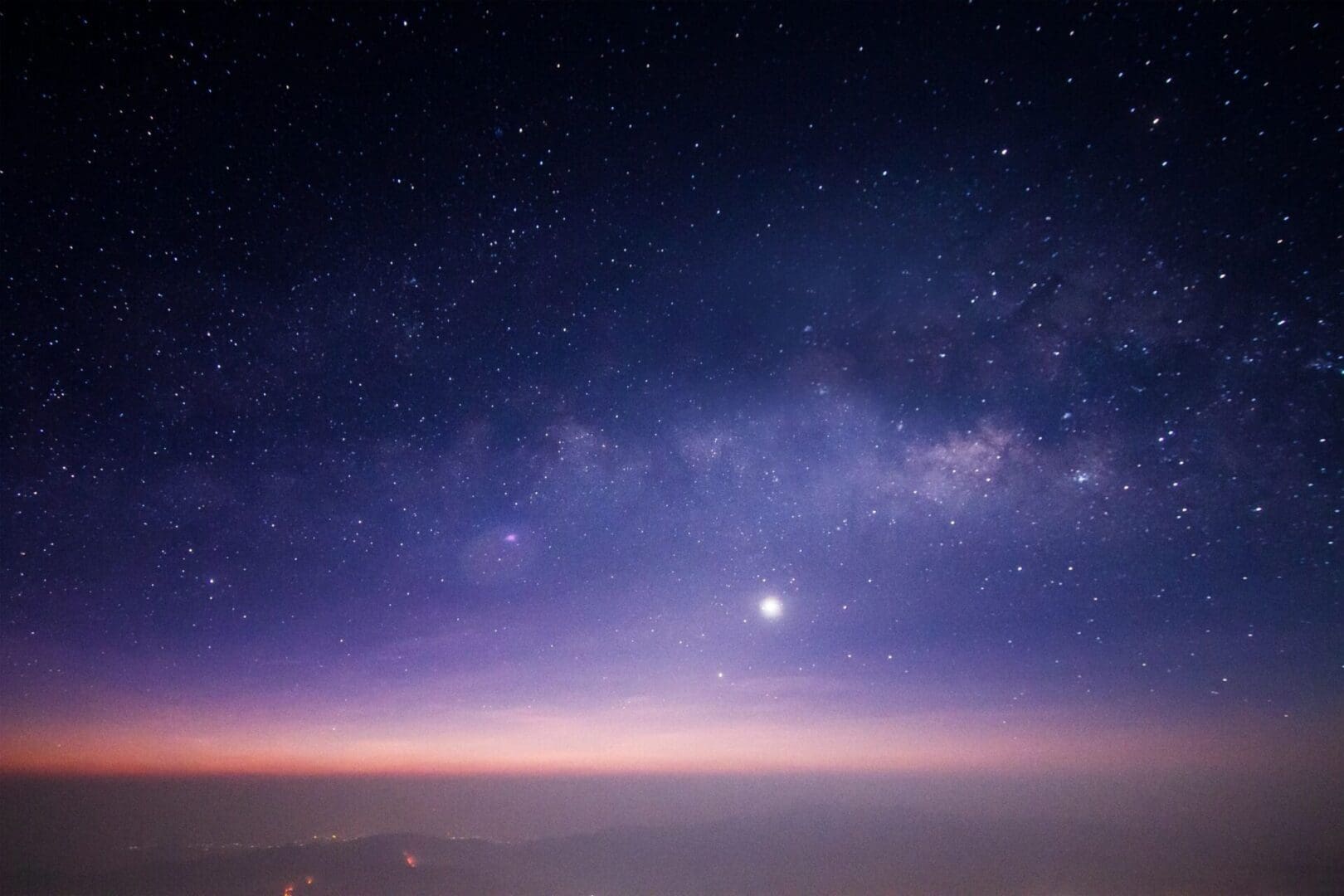Starry night sky with a bright celestial object and a colorful horizon.