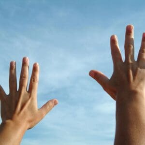 Two hands reaching up towards a clear blue sky.