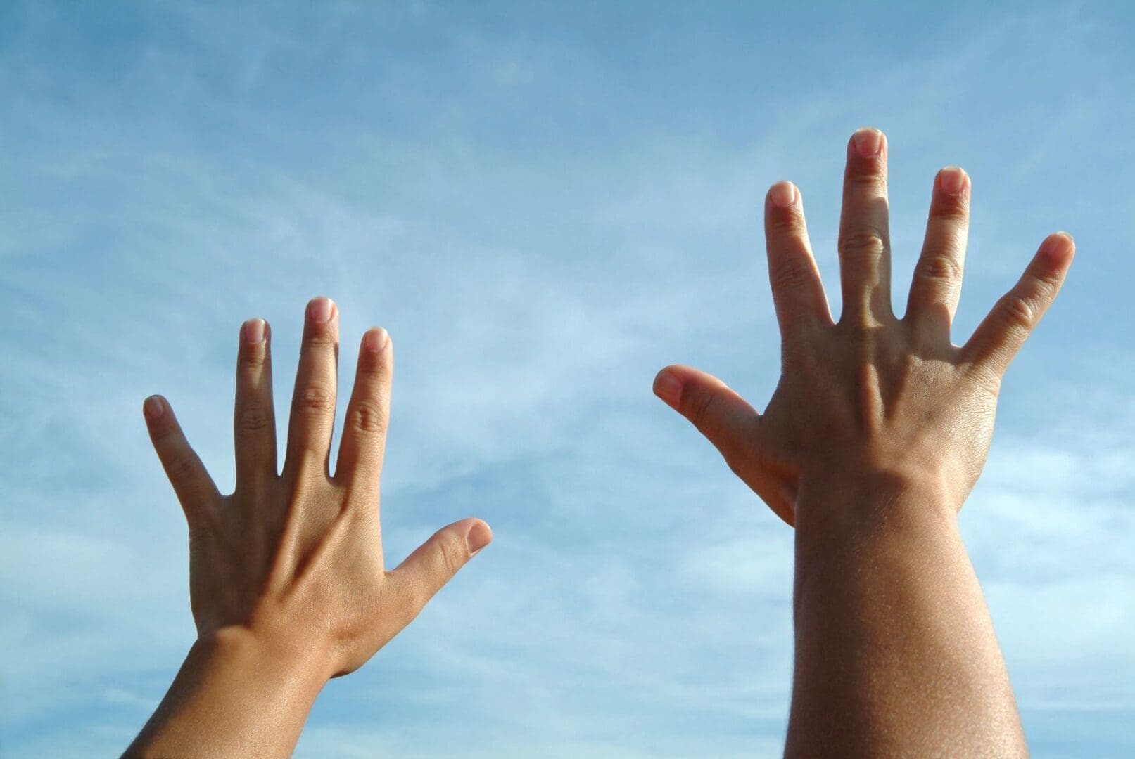 Two hands reaching up towards a clear blue sky.