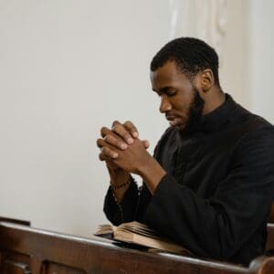 A man praying with hands clasped in a church pew.