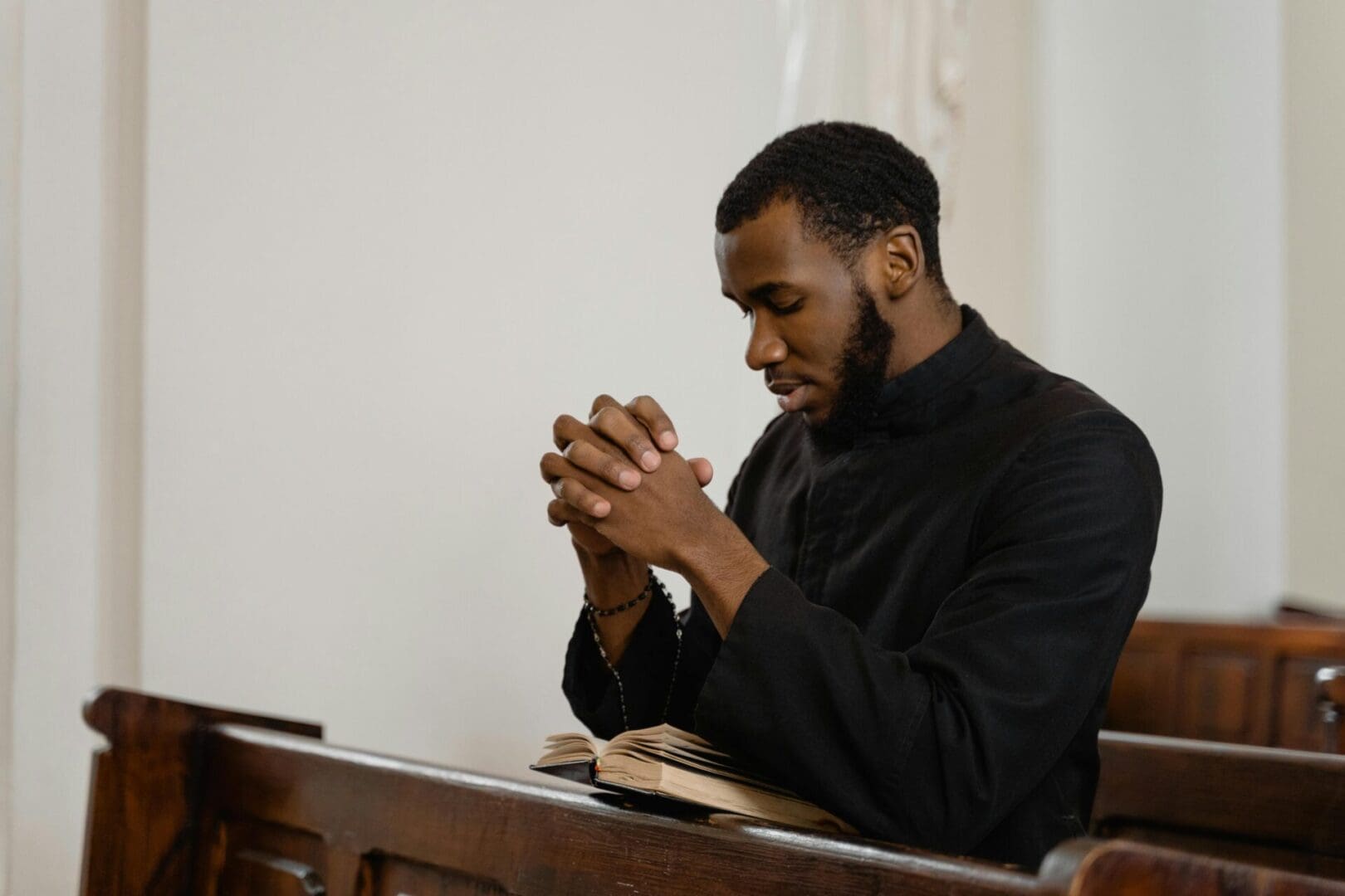 A man praying with hands clasped in a church pew.