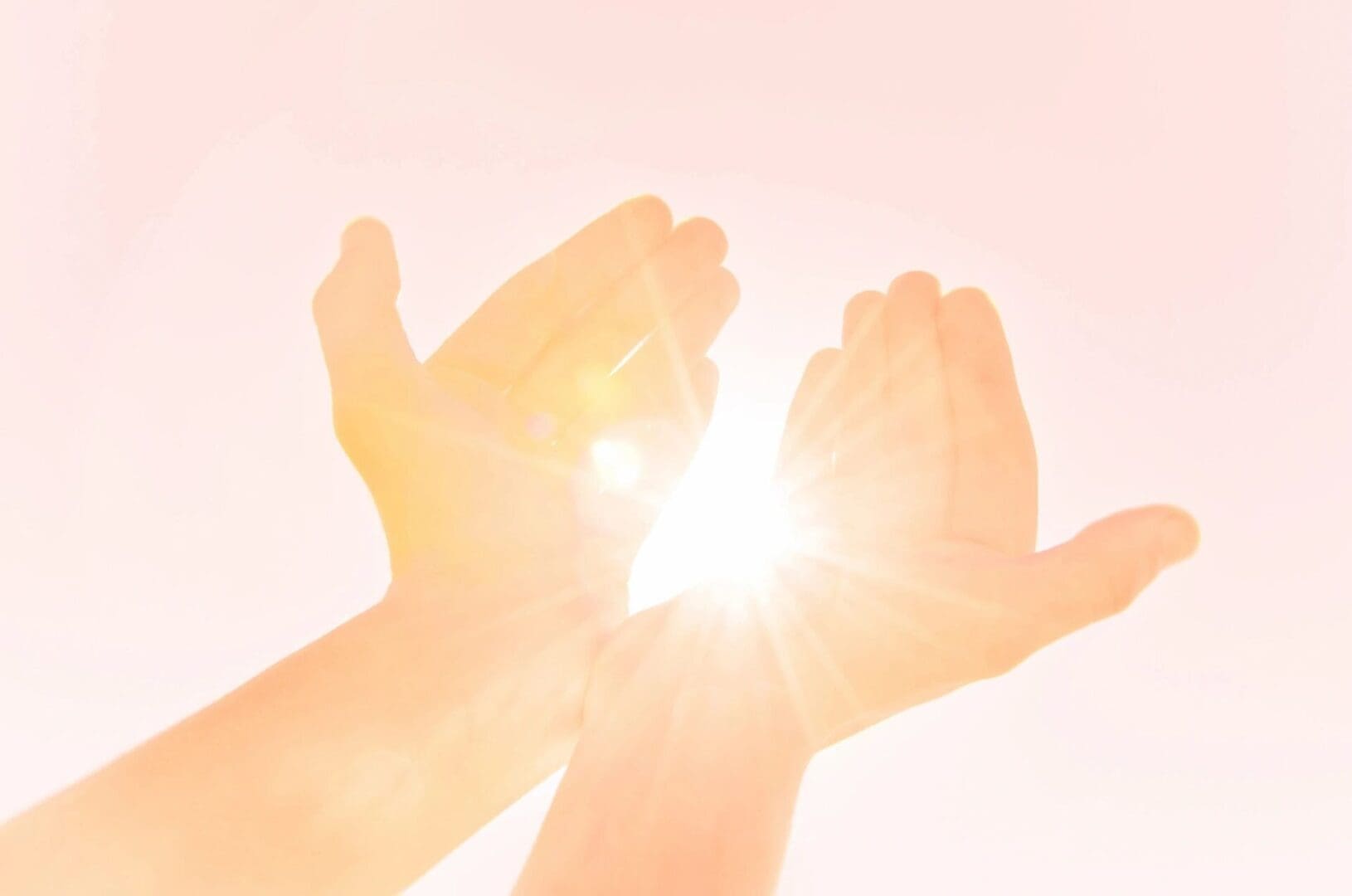 Hands cupping bright sunlight against a soft pink sky.