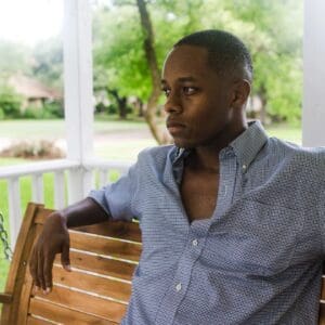 Man in casual shirt sitting on a wooden bench outdoors.