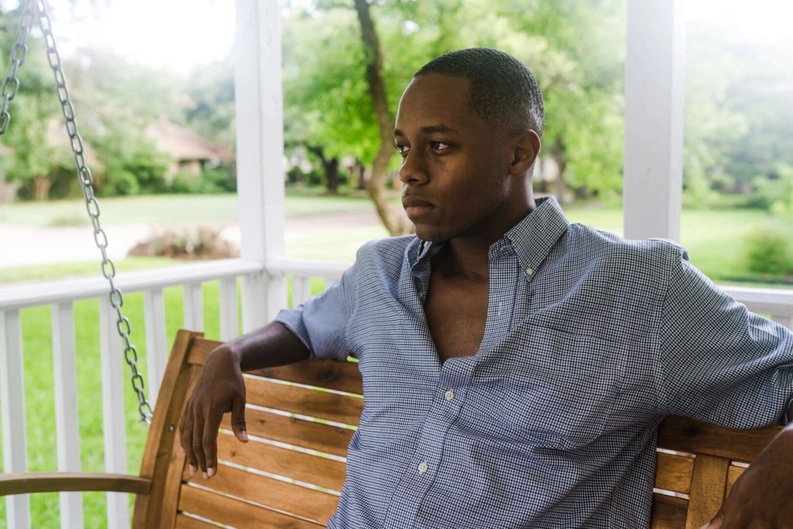 Man in casual shirt sitting on a wooden bench outdoors.