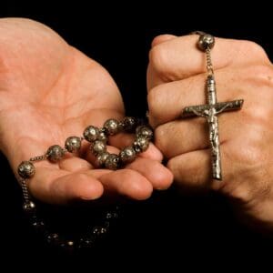 Hands holding a rosary with a crucifix.