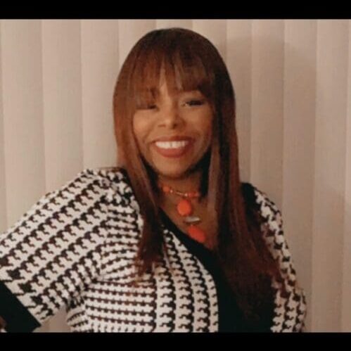 Smiling woman with straight hair and patterned jacket.