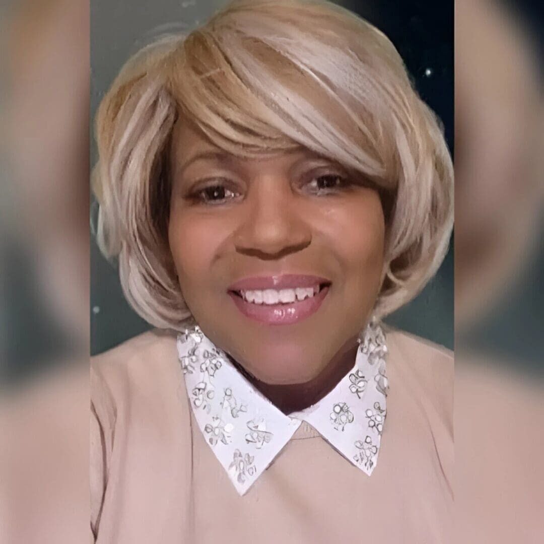 A smiling woman with short blonde hair and a white collared shirt.